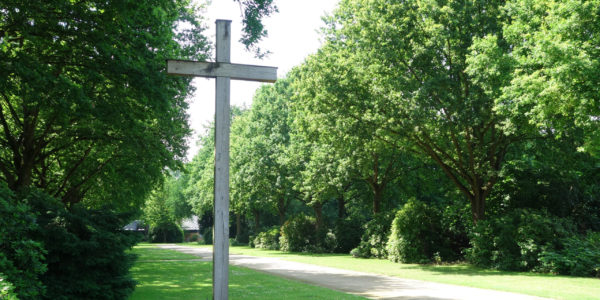 Blick auf ein Hochkreuz auf dem Friedhof Hassel-Oberfeldingen und eine Allee auf die Trauerhalle.