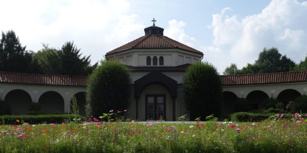 Das denkmalgeschütze Friedhofsgebäude auf dem Westfriedhof mit einer Blumenwiese im Vordergrund.